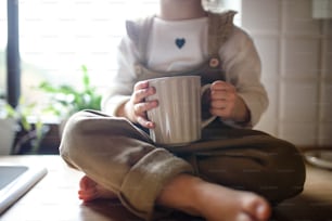 Midsection of toddler girl sitting on kitchen counter indoors at home, holding cup of tea.