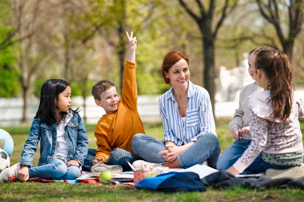 Ein Lehrer mit kleinen Kindern sitzt draußen im Stadtpark, Lerngruppen-Bildungskonzept.