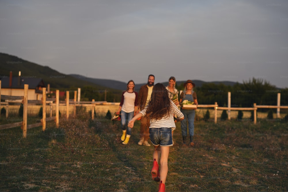 Una vista trasera de una niña corriendo hacia su familia al aire libre en una granja comunitaria.