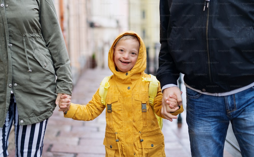 A down syndrome boy with unrecognizable parents outdoors on a walk in rain, holding hands.