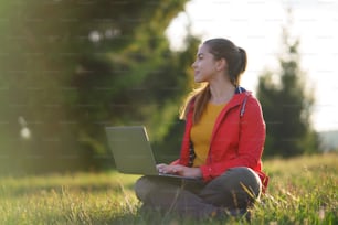 Side view of happy young woman using laptop in summer nature, outdoor office concept.