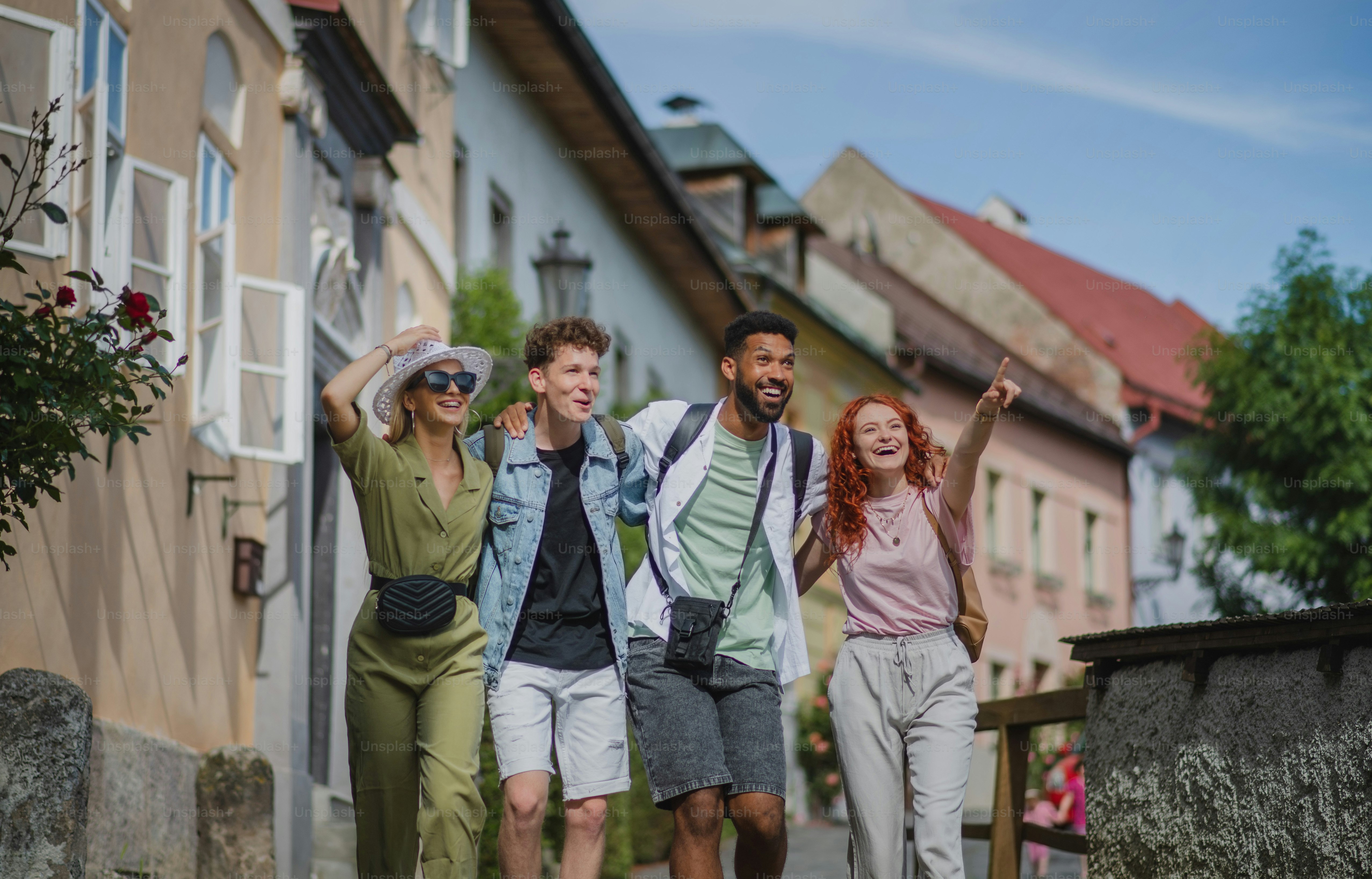 Eine Vorderansicht einer Gruppe glücklicher junger Leute im Freien auf einer Reise in der Stadt, Arm in Arm gehend.