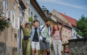 Uma vista frontal do grupo de jovens felizes ao ar livre em viagem na cidade, andando de braços dados.