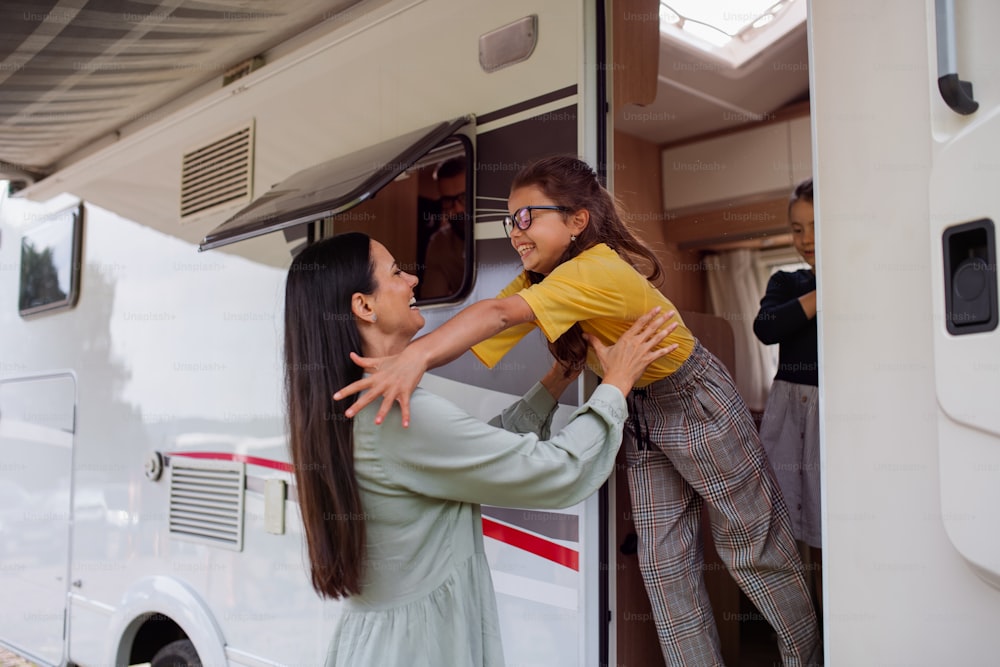 Uma mãe com filhas de pé de carro ao ar livre no acampamento ao entardecer, caravana viagem de férias em família.