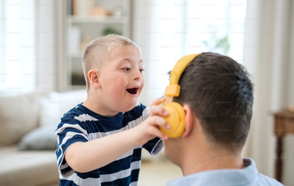 A happy down syndrome boy with father indoors at home, having fun with headphones.
