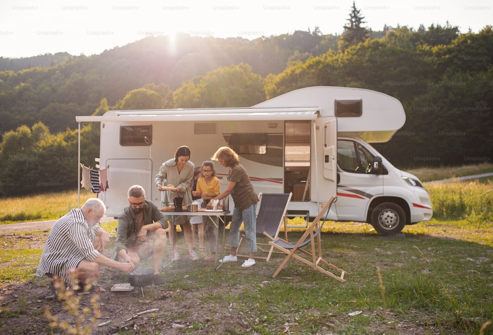 Una familia multigeneracional sentada y comiendo al aire libre en coche, viaje de vacaciones en caravana.