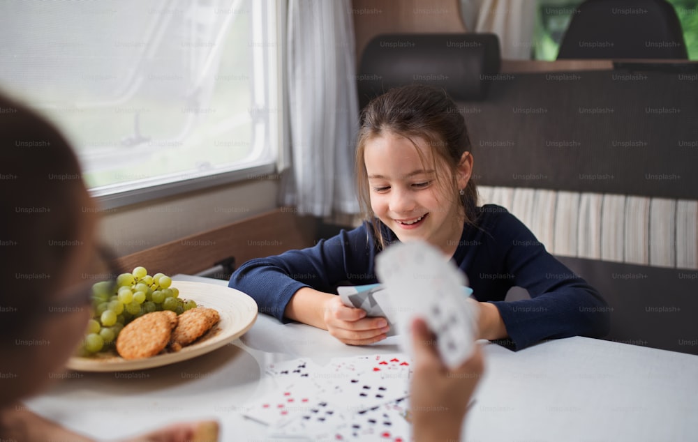 Meninas pequenas felizes jogando cartas dentro de casa na caravana, viagem de férias em família.