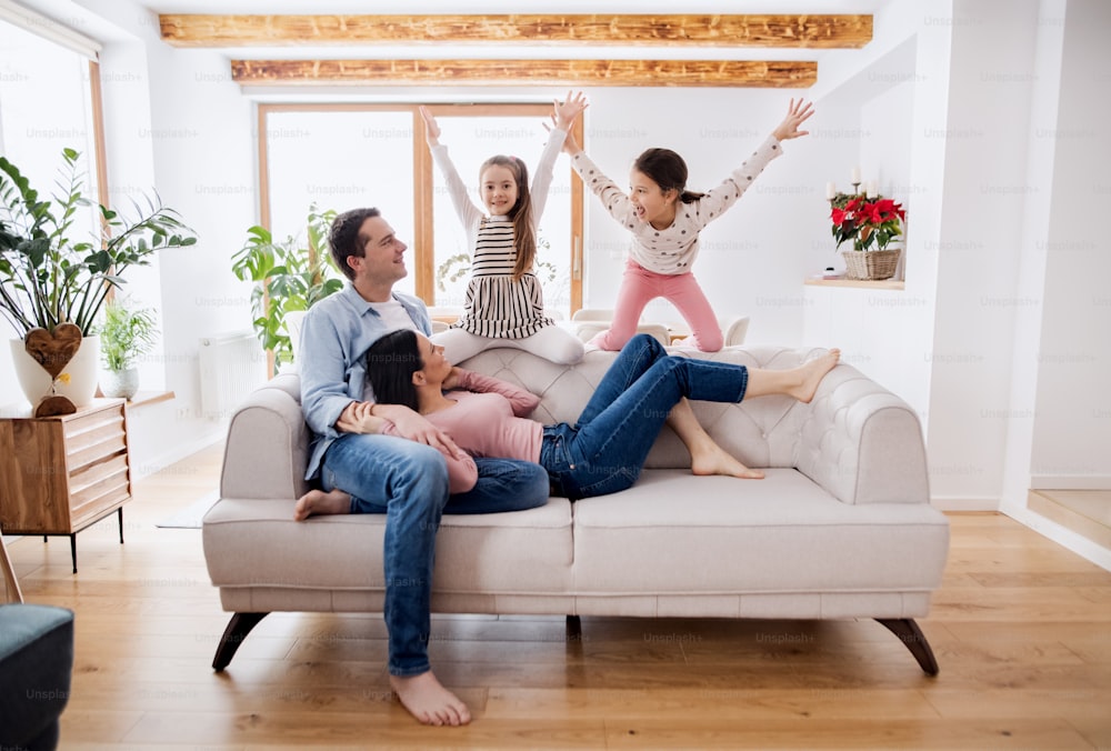 Retrato de padres con hijas pequeñas sentadas en el sofá en el interior de la casa, relajándose.