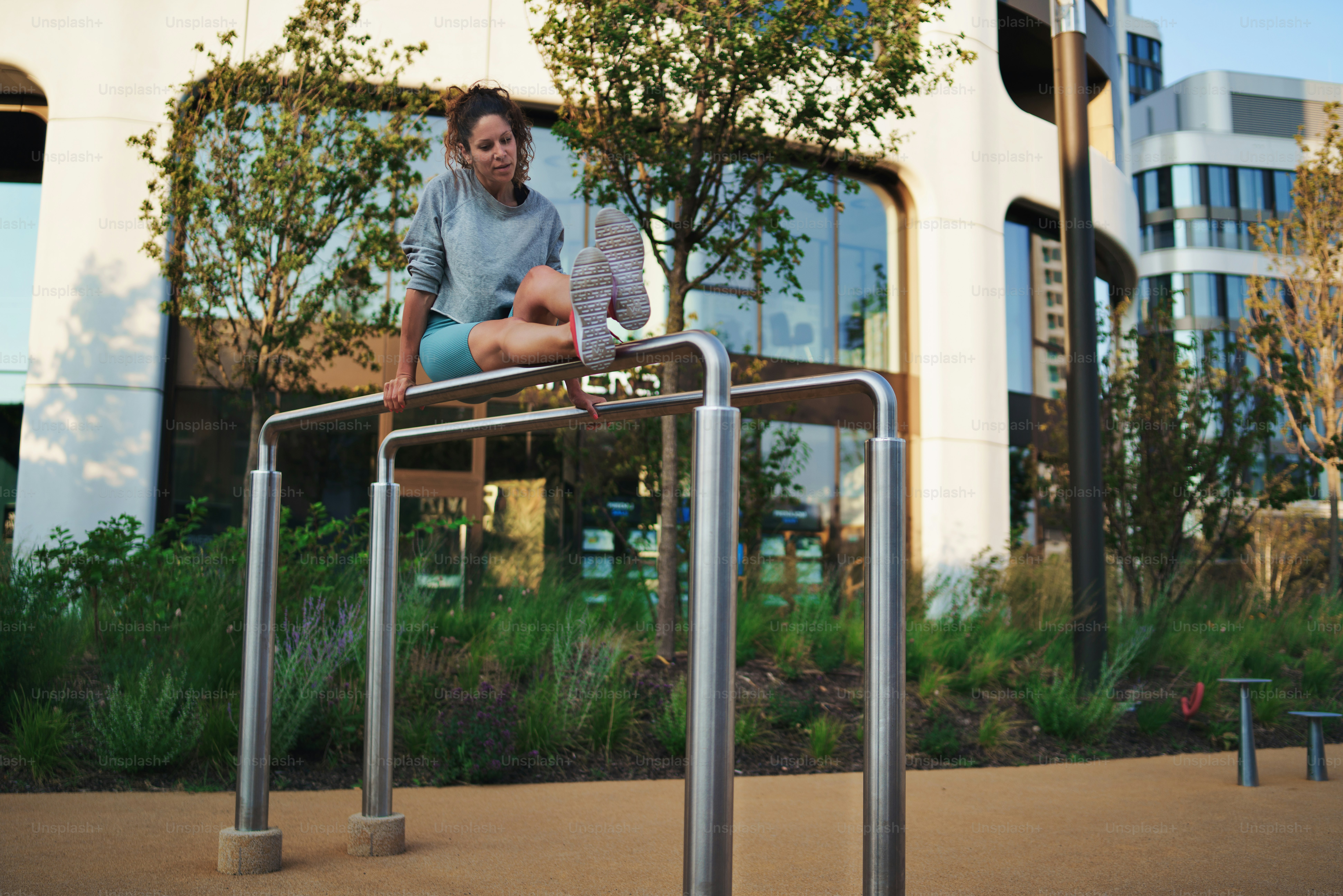 Happy mid adult woman doing exercise on parallel bars outdoors in city ...