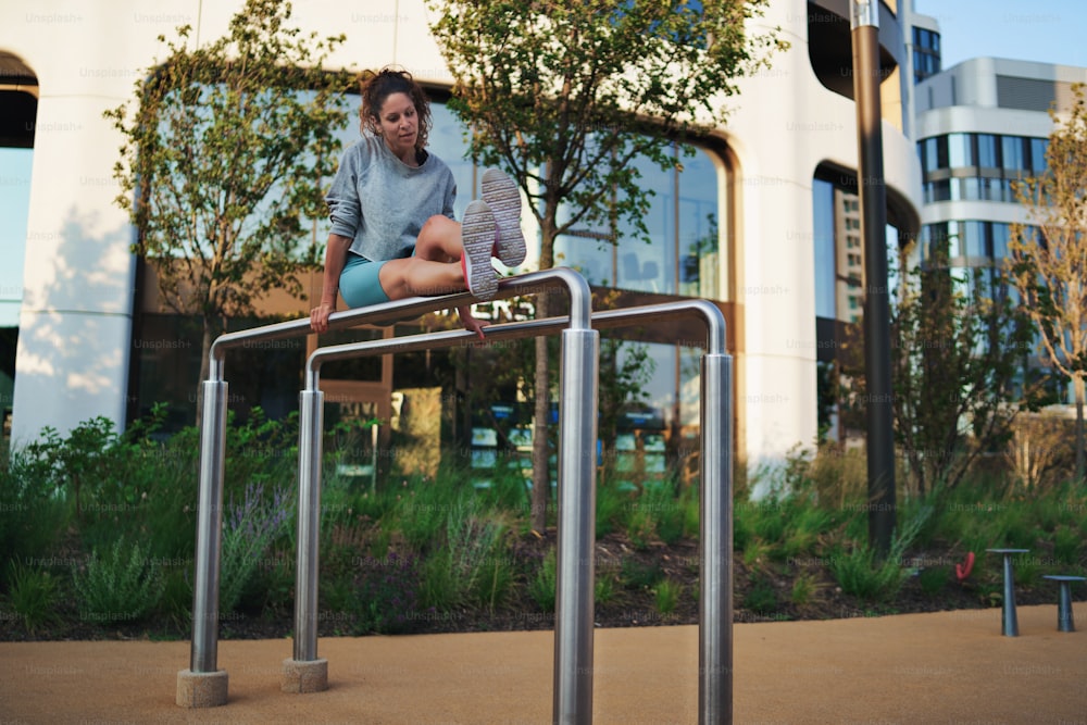 Femme adulte heureuse faisant de l’exercice sur des barres parallèles à l’extérieur en ville, concept de mode de vie sain.