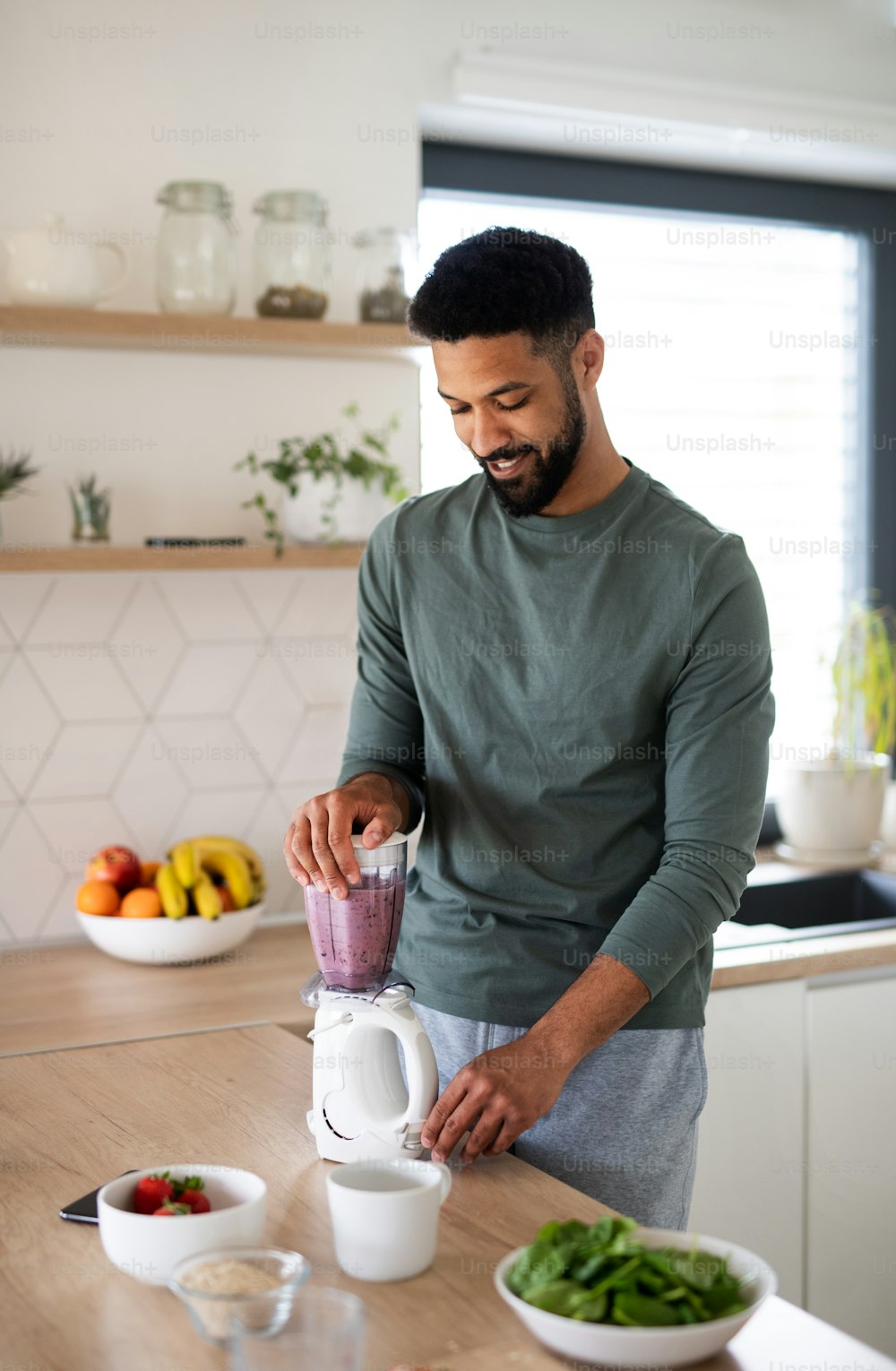 Portrait of young man with tablet preparing healthy breakfast indoors at home, making milk shake.