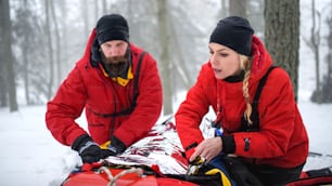 Los paramédicos del servicio de rescate de montaña realizan operaciones al aire libre en invierno en el bosque, con heridos en camilla.