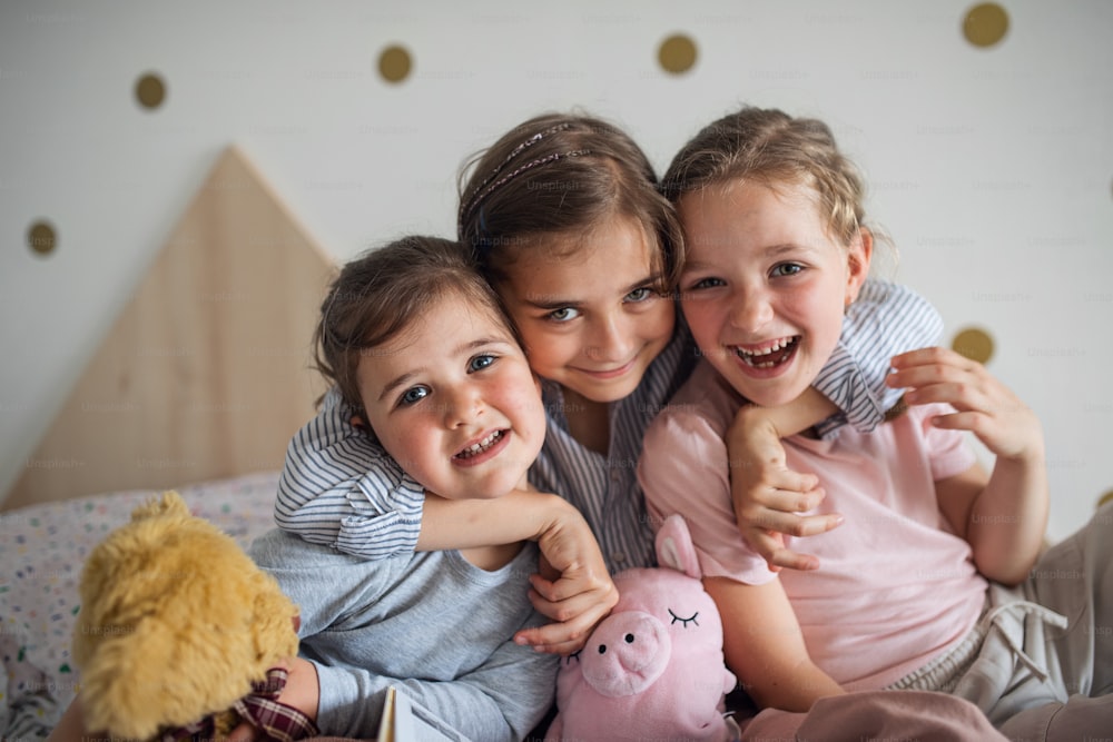 A portrait of three girls sisters indoors at home, looking at camera.