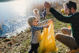 Padre maduro con niños pequeños recogiendo basura al aire libre en la naturaleza, concepto de plogging.