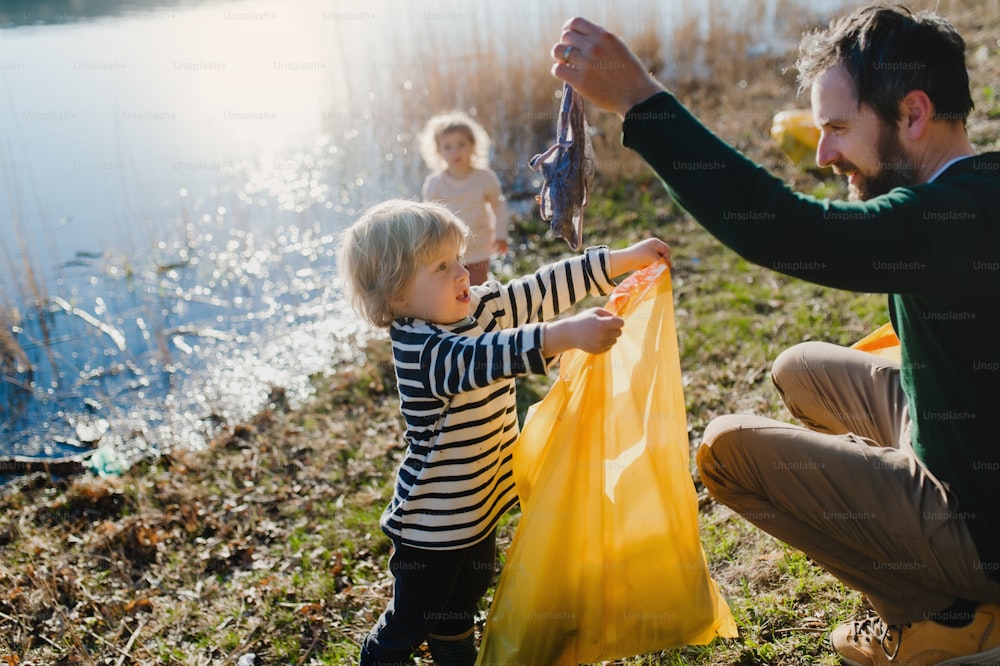 Pai maduro com crianças pequenas coletando lixo ao ar livre na natureza, conceito de plogging.