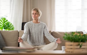 Ritratto di donna all'interno a casa che fa yoga, sul divano, salute mentale e concetto di meditazione.