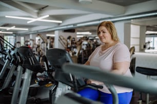 Eine glückliche mittelgroße übergewichtige Frau, die drinnen im Fitnessstudio auf Stepper trainiert