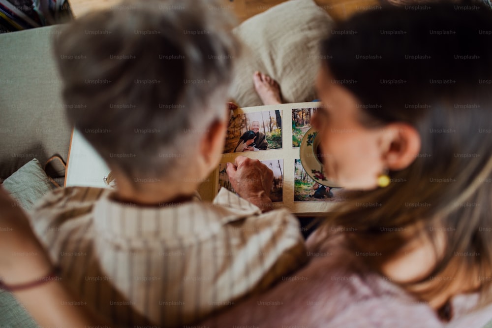 Une vue de dessus d’une mère âgée avec sa fille adulte à l’intérieur de la maison, regardant des photos de famille.