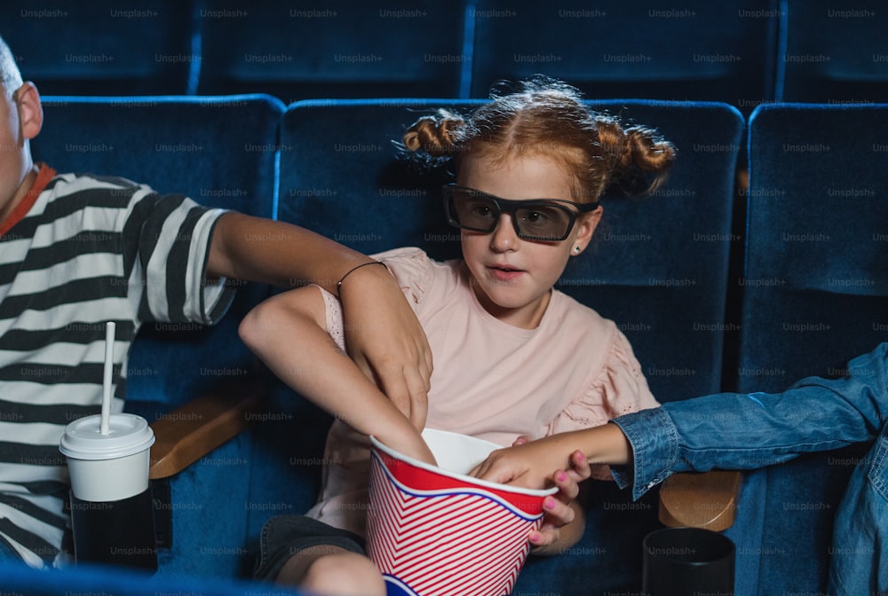Happy small children with 3d glasses and popcorn in the cinema, watching film and eating popcorn.