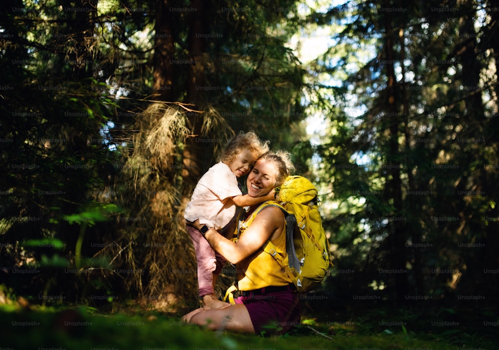 夏の自然の中で小さな娘を連れた幸せな母親が屋外で抱き合って休んでいる横から。