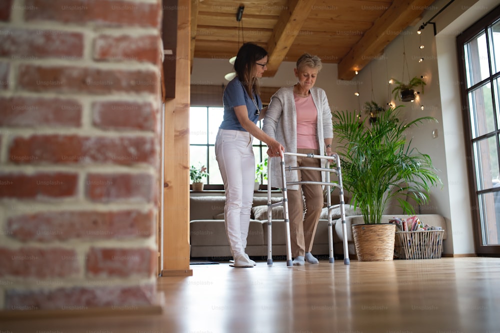 A healthcare worker or caregiver visiting senior woman indoors at home, helping her to walk.