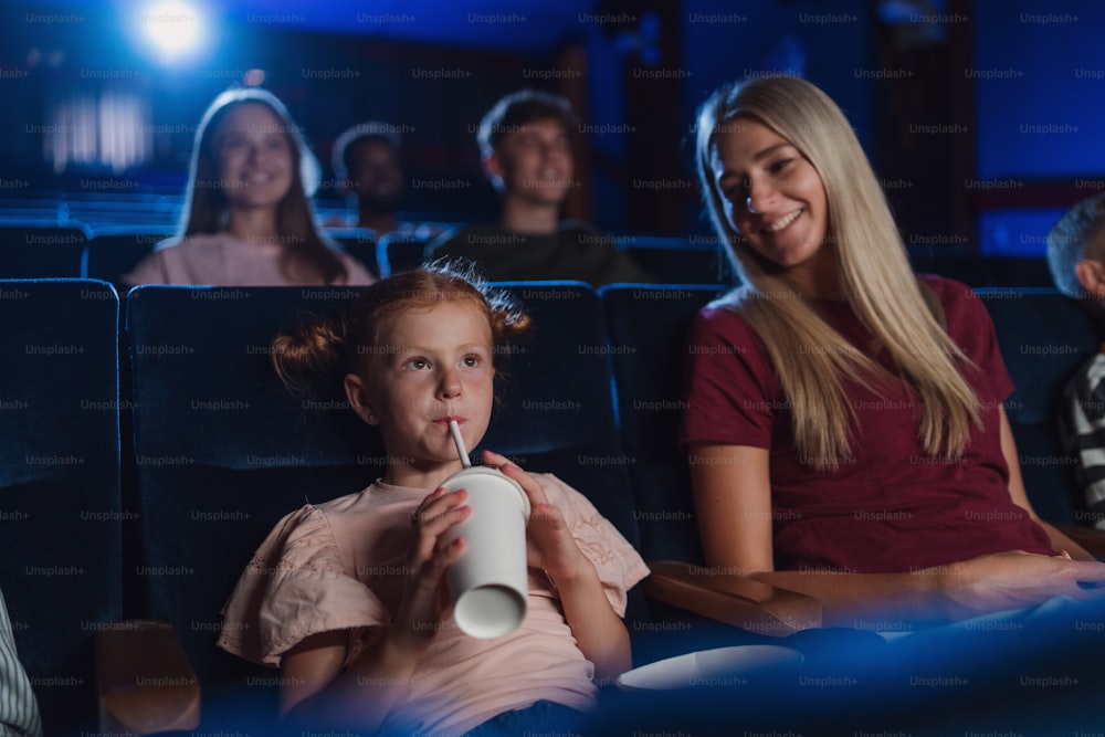 A mother with happy small children in the cinema, watching film and drinking with a straw.