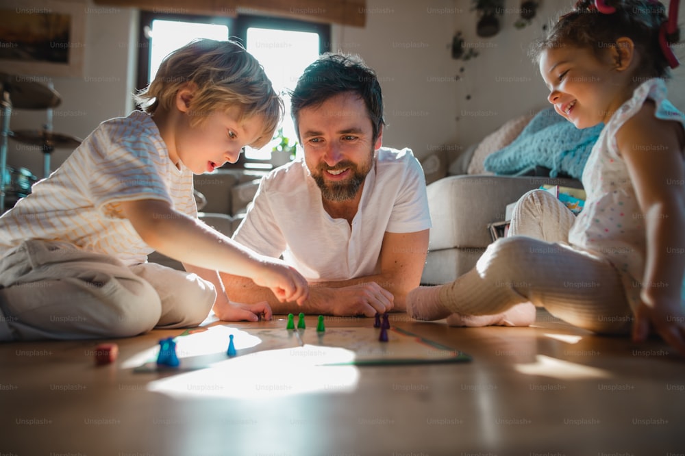 Ein reifer Vater mit zwei kleinen Kindern, die sich drinnen zu Hause ausruhen und Brettspiele spielen.