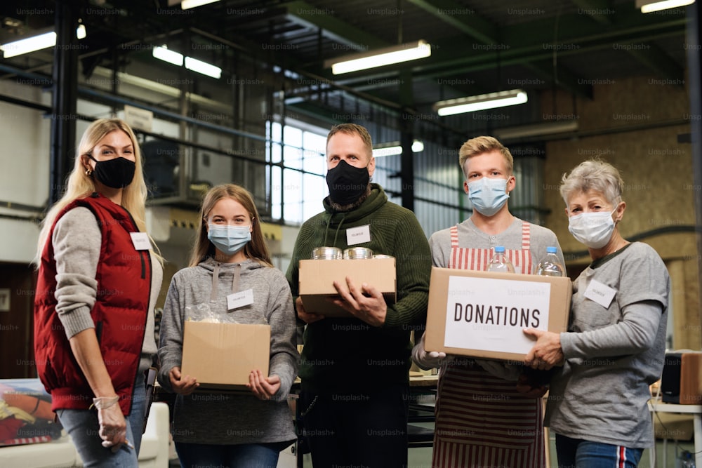 Gruppe von Freiwilligen mit Boxen, die in die Kamera im gemeinnützigen Spendenzentrum der Gemeinde schauen, Coronavirus-Konzept.