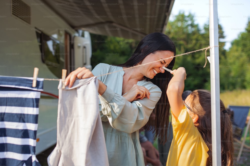 Uma mãe com a filha pendurando roupas de carro ao ar livre no acampamento, caravana viagem de férias em família.