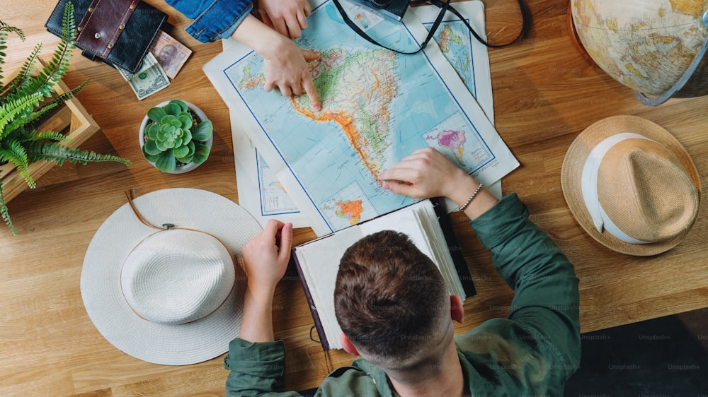 Vista superior de una pareja joven irreconocible con mapas que planifican el viaje de vacaciones, concepto de viaje de escritorio.