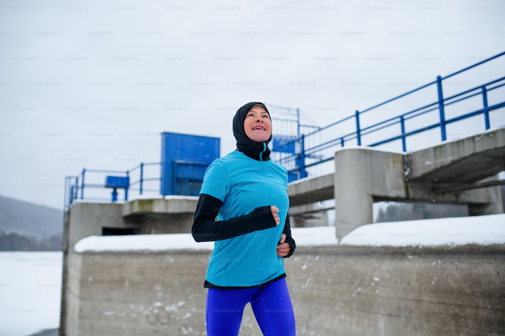 눈 덮인 겨울, 추운 날씨에 야외에서 달리는 행복한 활동적인 노인 여성.