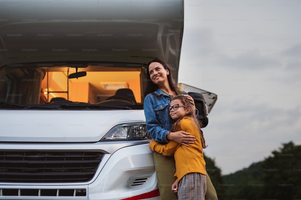 Glückliche Mutter mit Tochter steht mit dem Auto draußen auf dem Campingplatz in der Abenddämmerung, Wohnwagen Familienurlaub.