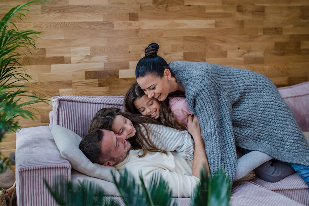 Due sorelle felici che si divertono con un padre e una madre, sdraiate sul divano di casa.