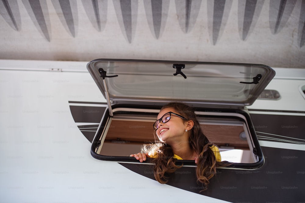 Uma menina pequena feliz olhando para fora através da janela da caravana, viagem de férias em família.