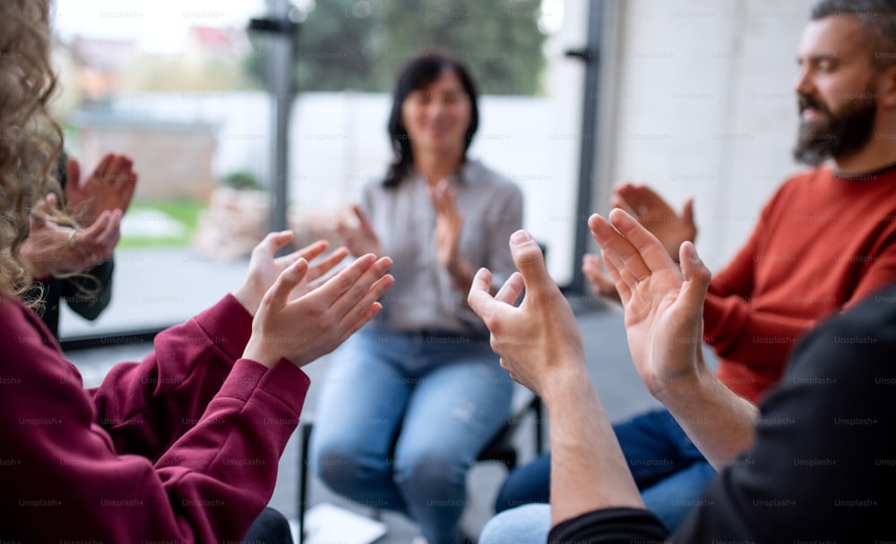 Des hommes et des femmes assis en cercle pendant une thérapie de groupe, applaudissent.