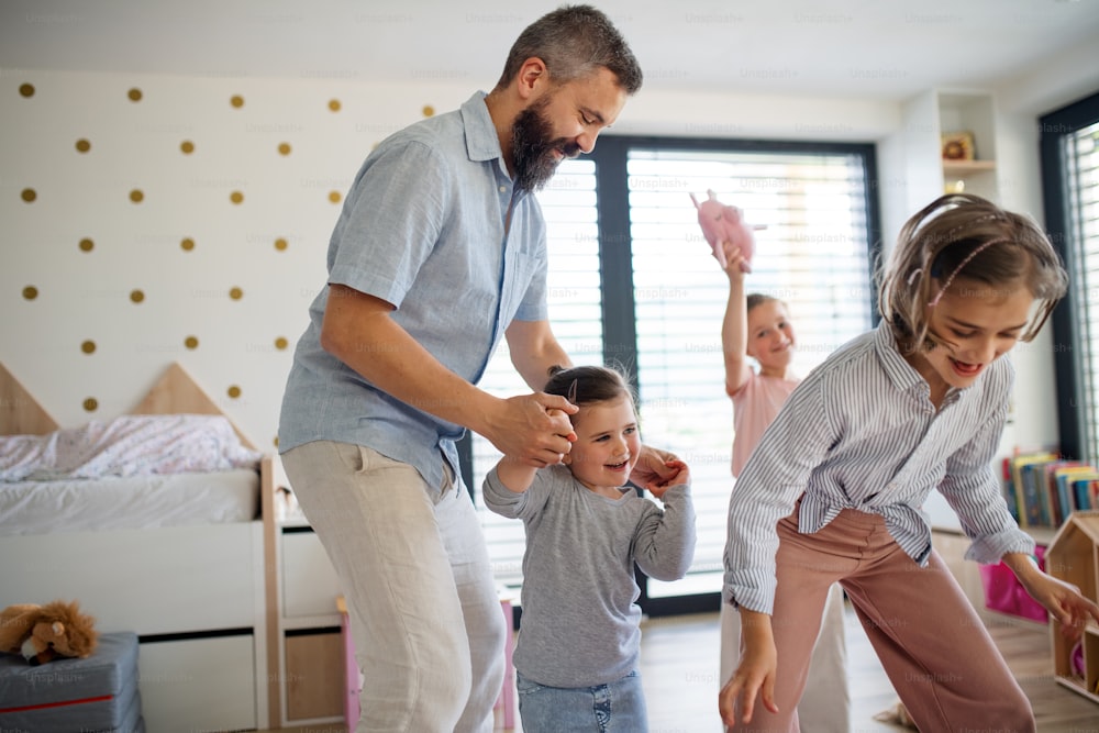 A father with three daughters indoors at home, playing and holding hands. photo – People Image on Unsplash