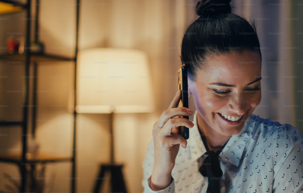A close-up of happy business woman talking on phone in office at night.