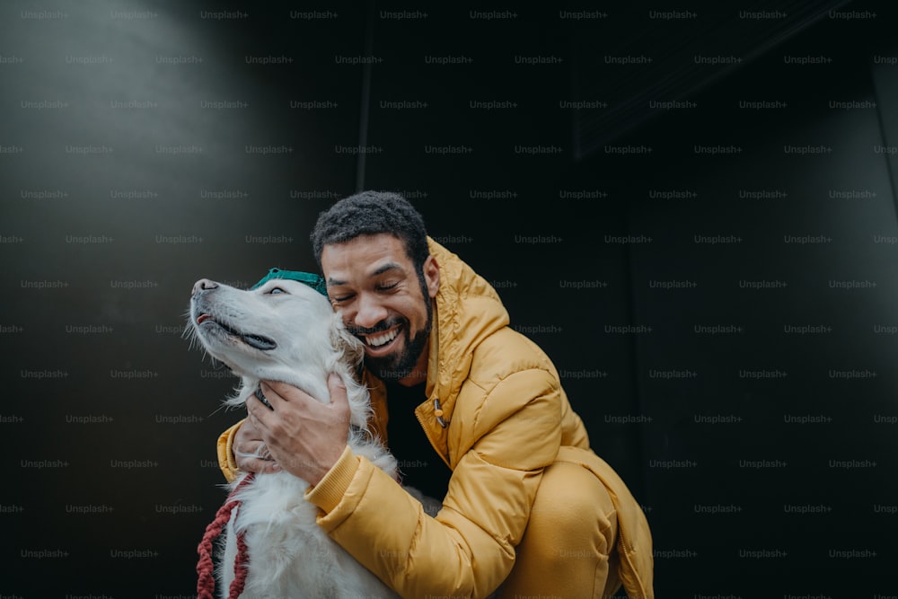 Ein glücklicher junger Mann umarmt seinen Hund im Winter draußen vor dunklem Hintergrund.