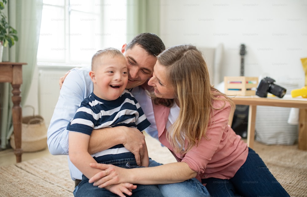 Um menino alegre com síndrome de down com os pais dentro de casa abraçados, rindo.