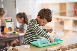 Small concentrated nursery school boy playing indoors in classroom, montessori learning.