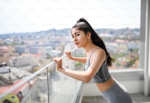 Un portrait de jeune femme sportive faisant de l’exercice sur le balcon à l’extérieur en ville, s’étirant.