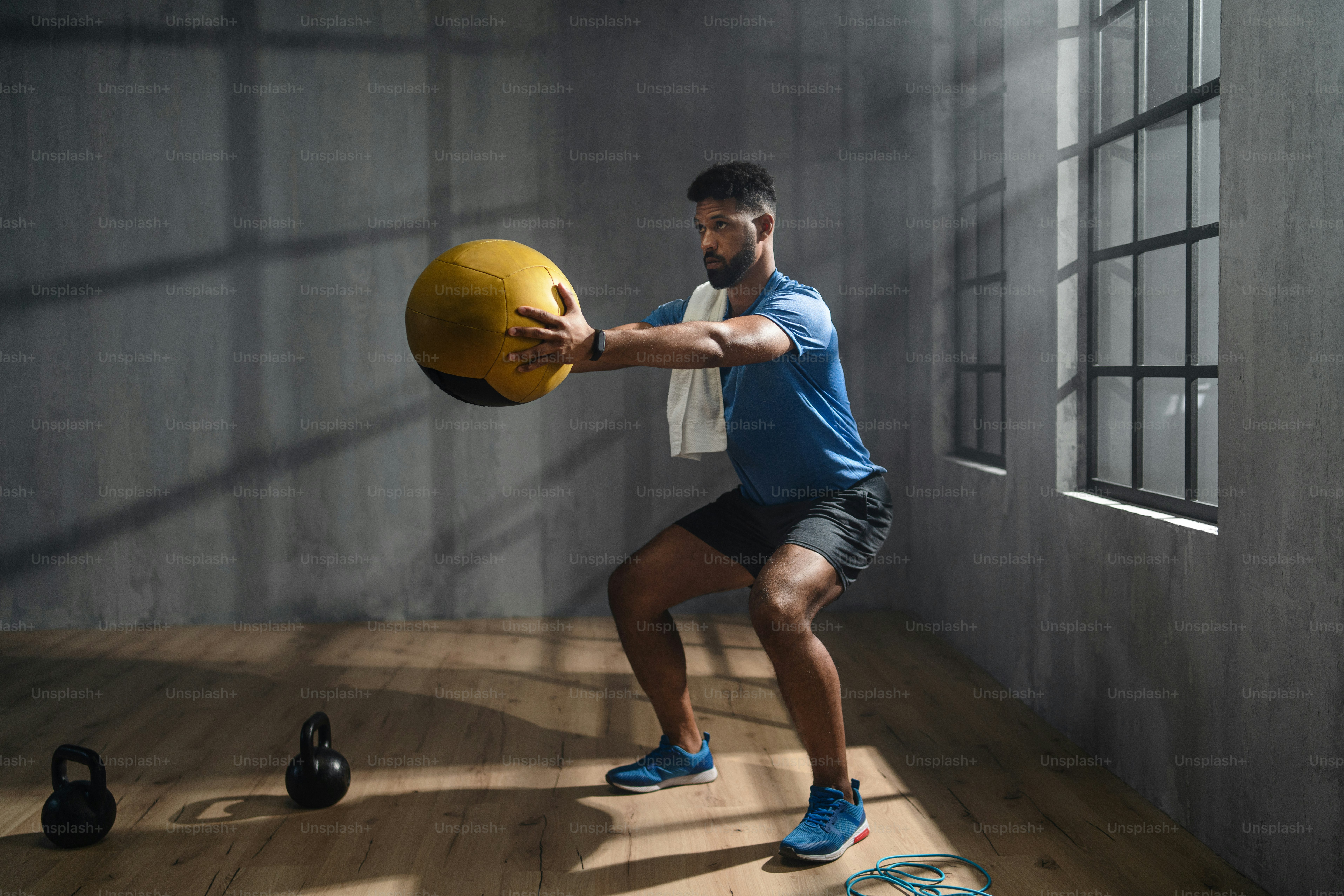 A young African American sportsman standing and lifting a medicine ball indoors, training concept.
