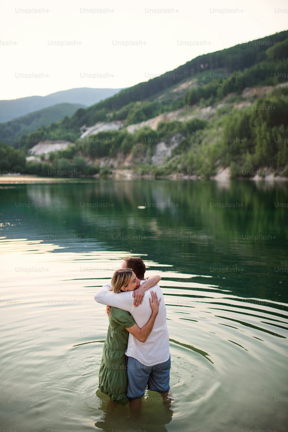 A mature couple in love standing in water in lake in nature, hugging.