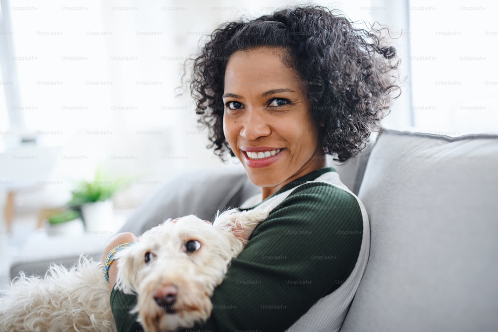 A portrait of happy mature woman with dog sitting indoors at home, looking at camera.