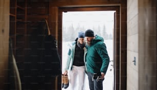 Portrait of mature couple entering wooden hut, holiday in winter nature concept.