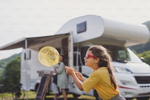 A happy small girl standing outdoors with butterfly net by caravan car, family holiday trip.