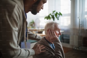 A caregiver helping seniot man to insert hearing aid in his ear.