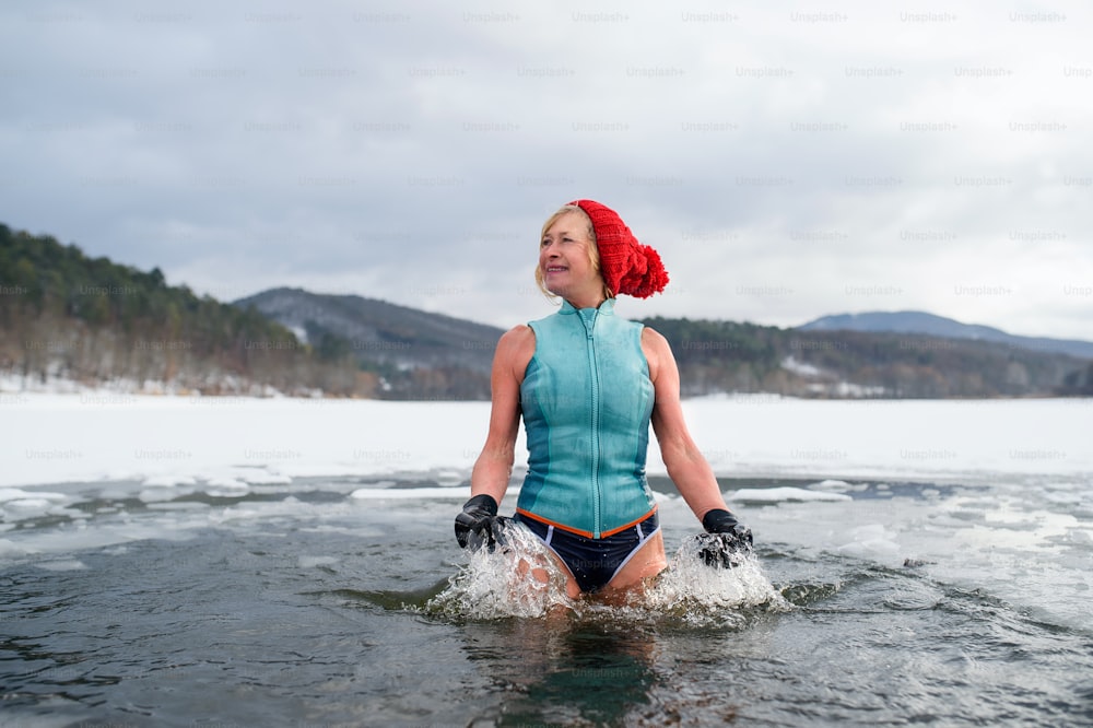 Niedrige Winkelansicht einer aktiven Seniorin im Badeanzug im Freien im Winter, Kältetherapiekonzept.