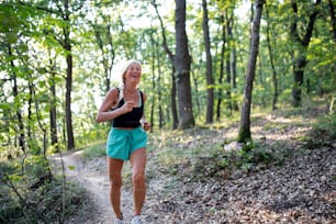 Una donna anziana attiva felice che fa jogging all'aperto nella foresta.