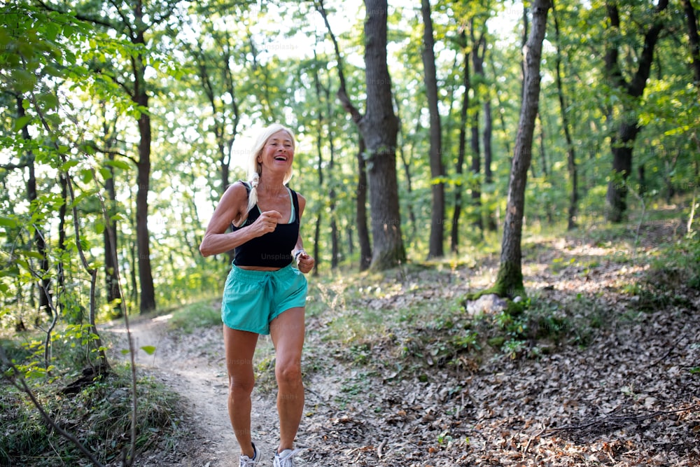 A happy active senior woman jogging outdoors in forest.